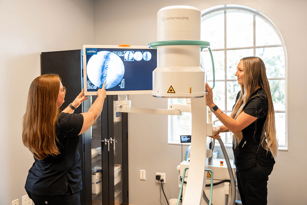 Two female healthcare professionals operating a Ziehm Imaging C-arm machine while reviewing spinal X-ray images in a modern medical facility